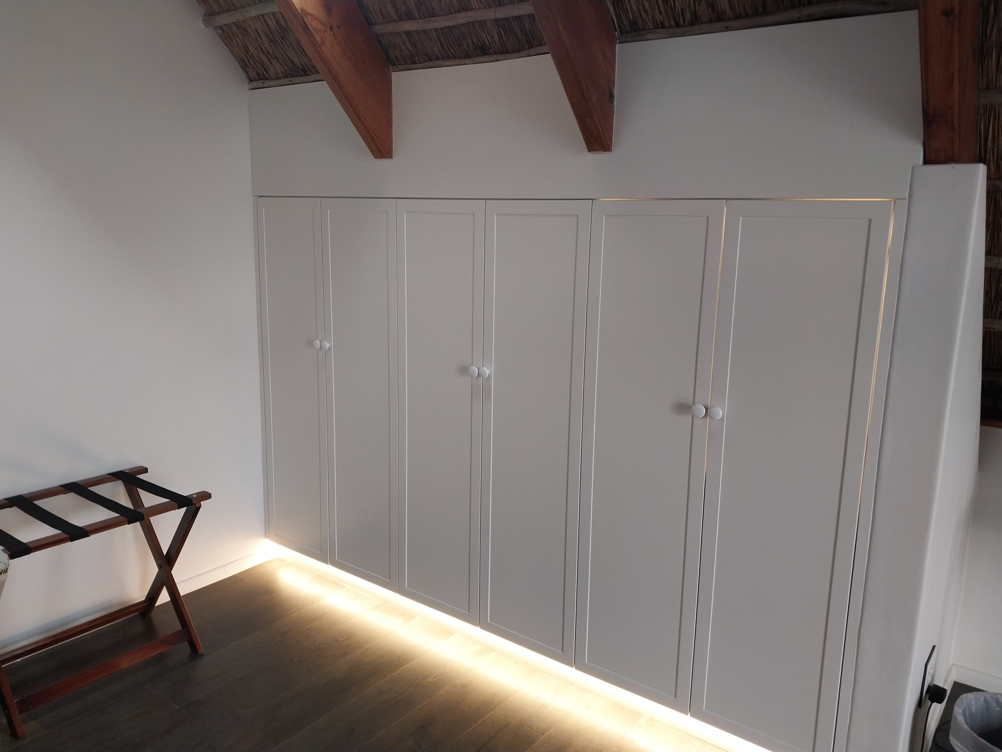 Painted built-in wardrobe with LED uplighting in thatched bedroom